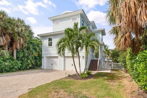 A two-story house with a garage, surrounded by palm trees and a well-maintained lawn. - Coastal Livin' by Duncan Real Estate (Holmes Beach)