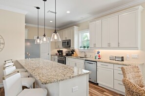 Una cocina moderna con armarios blancos, encimeras de granito e iluminación colgante.