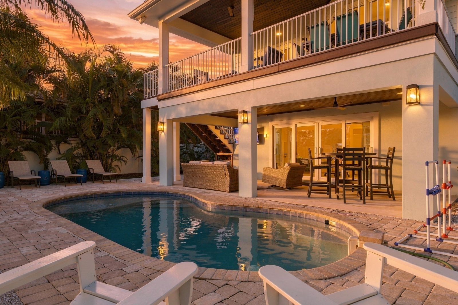A pool area with lounge chairs, a covered seating area, and a staircase leading to a balcony.