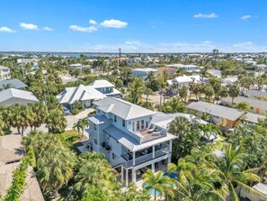 A large two-story house with a balcony, surrounded by palm trees and a view of the ocean. - Coastal Livin' by Duncan Real Estate (Holmes Beach)