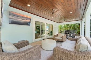 A covered outdoor seating area with wicker furniture, a large window, and a ceiling fan. - Coastal Livin' by Duncan Real Estate (Holmes Beach)