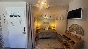 Ett sovrum med en säng, sänglampor, en tv, ett träskåp och en dörr med krokar.