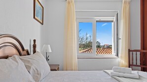 En pænt redt seng med trægavl, et natbord med lampe, og et vindue med gardiner.