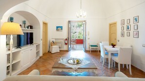 Een kamer met een eettafel, stoelen, een kroonluchter, een televisie en een open haard.