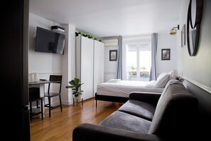 A bedroom with a bed, a desk with a chair, a TV mounted on the wall, and a balcony with curtains. - Nice renovated AC studio in Saint Germain (Paris)