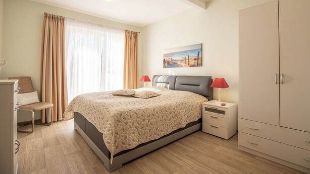 A bedroom with a bed, bedside tables, a wardrobe, and a window with curtains. - Haus Nordseekrabbe Apartment 11 46m2 Terrace Wheelchair accessible Category 2 (Neuharlingersiel)