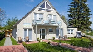 A two-story building with a balcony, a small porch, and a flag indicating it is a hotel. - Haus Nordseekrabbe Apartment 11 46m2 Terrace Wheelchair accessible Category 2 (Neuharlingersiel)