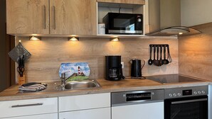 A modern kitchen with wooden cabinets, a Bosch microwave, a coffee maker, and a dishwasher. - Haus Nordseekrabbe Apartment 11 46m2 Terrace Wheelchair accessible Category 2 (Neuharlingersiel)
