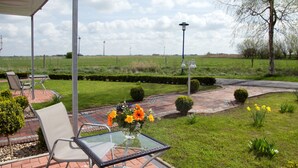 A patio with outdoor furniture, a glass table, and a flower arrangement. - Haus Nordseekrabbe Apartment 11 46m2 Terrace Wheelchair accessible Category 2 (Neuharlingersiel)