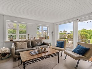 A spacious room with a large window, a leather sofa, a wooden coffee table, and a chair with blue cushions. - "Bo" - 250m from the sea by Interhome (Hadsund)