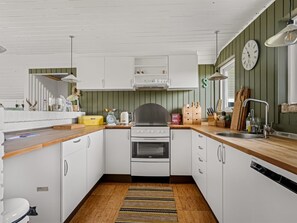 Une cuisine de taille réduite, avec des meubles blancs, une cuisinière, un évier et une horloge au mur.