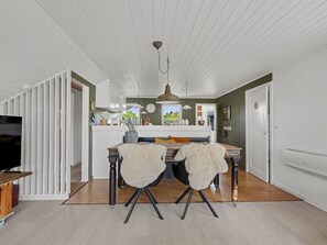 A dining area with a wooden table, two chairs, a hanging pendant light, and a kitchen in the background. - "Bo" - 250m from the sea by Interhome (Hadsund)