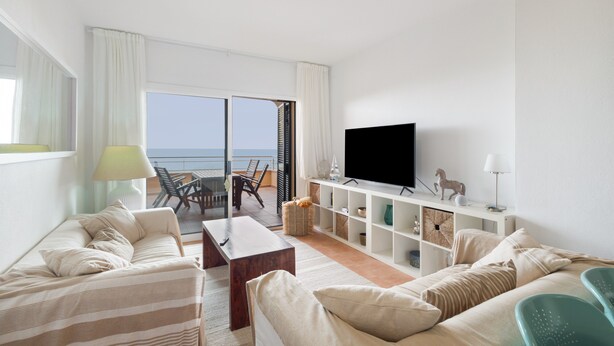A modern living room with a sofa, a coffee table, a TV, and a balcony with a view of the sea. - Apartment 'Sa Calma 2 - 1D' with Sea View, Wi-Fi and Air Conditioning (Begur)