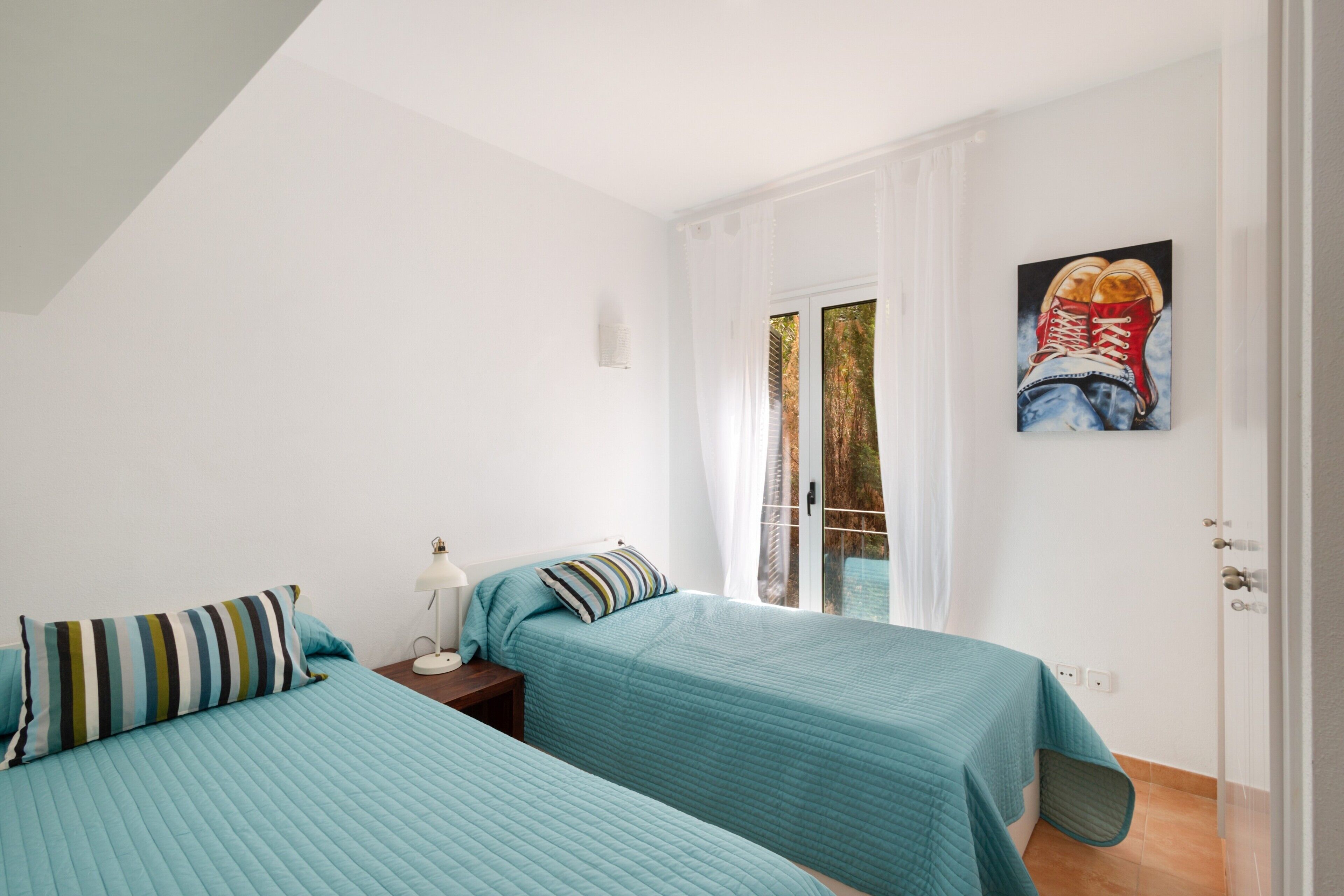 Een slaapkamer met twee bedden, een nachtkastje, een schilderij en een raam met gordijnen.