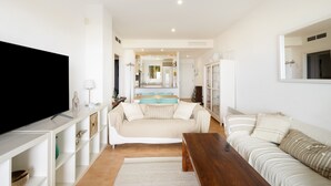A living room with a TV, sofa, coffee table, and a kitchen in the background. - Apartment 'Sa Calma 2 - 1D' with Sea View, Wi-Fi and Air Conditioning (Begur)