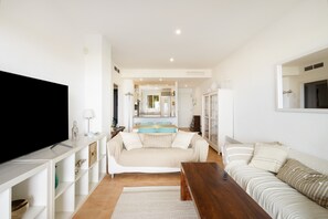 A living room with a TV, sofa, coffee table, and a kitchen in the background. - Apartment 'Sa Calma 2 - 1D' with Sea View, Wi-Fi and Air Conditioning (Begur)