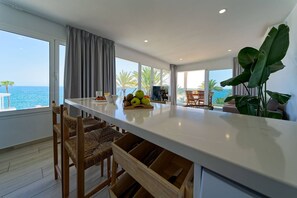 A modern kitchen with a central island, dining area with chairs, large windows with ocean views, and a plant. - 3.3 Deva Beach - Oceanview luxury 1 bedroom Apartm (Maspalomas)