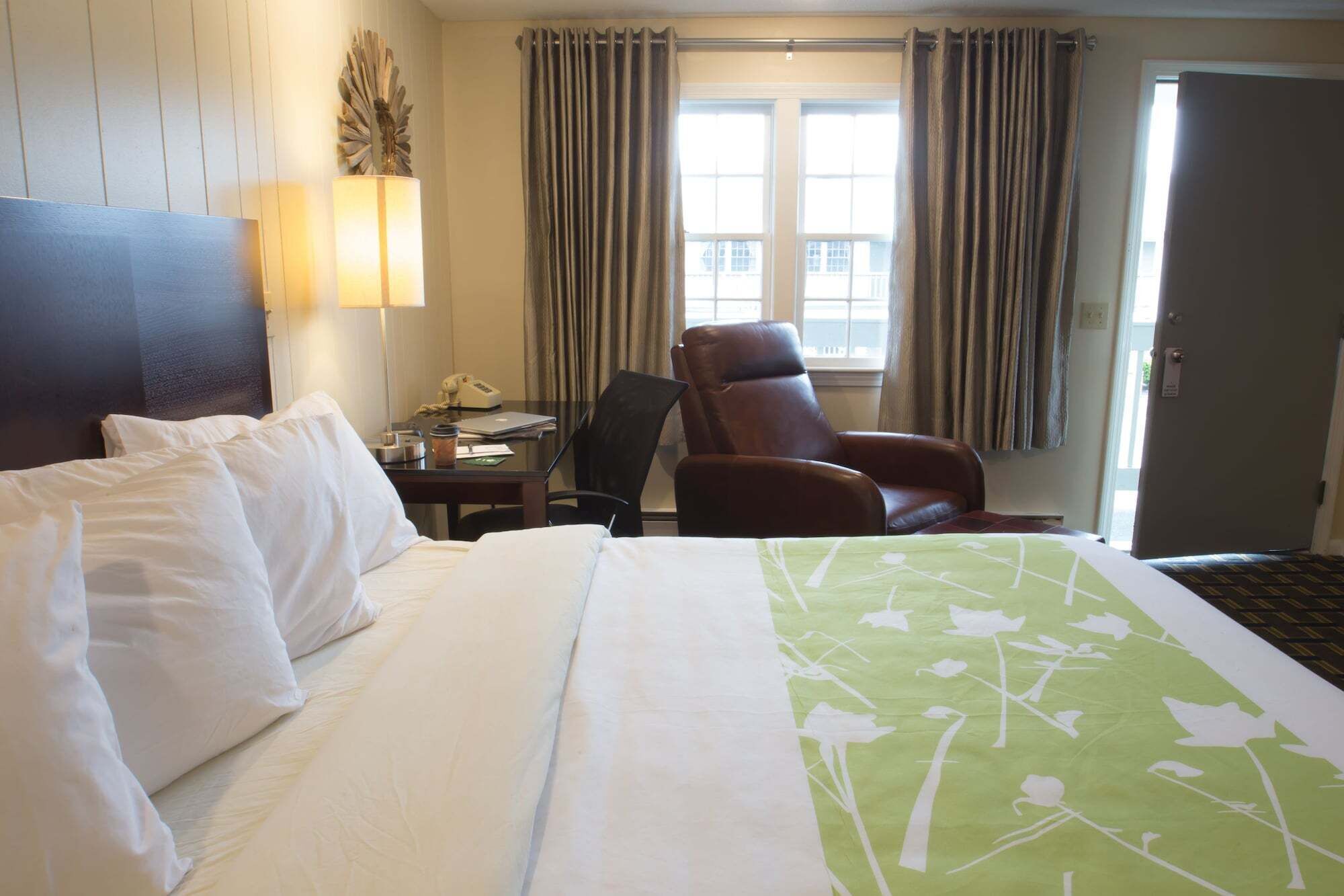 A hotel room with a bed, a desk, a chair, and a window with curtains.