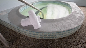 Un jacuzzi con borde de azulejos, una toalla blanca en el borde y señales de advertencia en las paredes.