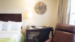 Una habitación de hotel con una cama, un escritorio con lámpara, una silla y un espejo adosado a la pared.