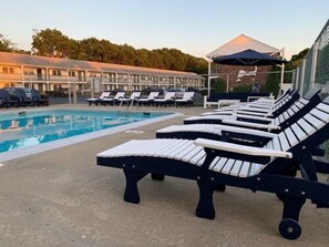 Zona junto a la piscina con sillones, una piscina y un edificio al fondo.
