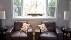 Una habitación con dos sofás de cuero, una ventana con vista a un velero y dos lámparas sobre mesitas.