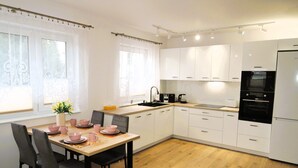 A modern kitchen with white cabinets, a wooden dining table, and a black oven. - New apartment in Wisełka (Wisełka)