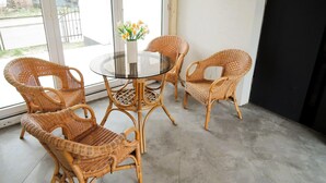A room with wicker chairs around a glass table, a vase with flowers, and a view through large windows. - New apartment in Wisełka (Wisełka)