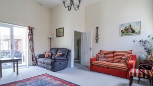 Ett vardagsrum med en soffa, en fåtölj, en matta och en dörr som leder till ett annat rum.