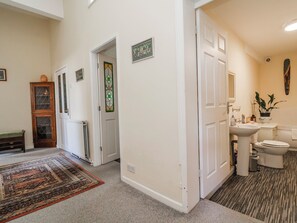 Un passadís amb un rug ornamental, un armari de fusta, una porta amb un disseny de vitrall i un bany amb un lavabo i un vàter.
