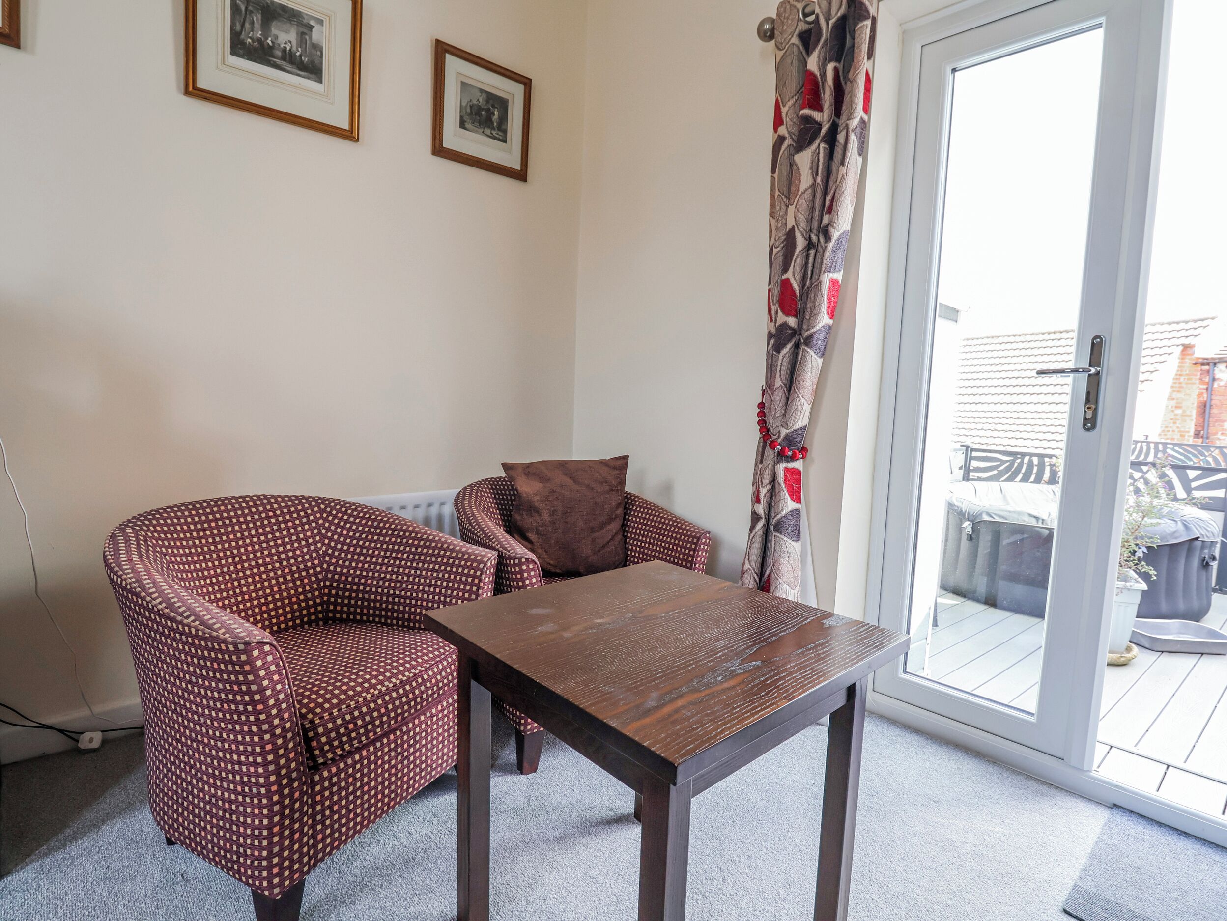 A room with a patterned armchair, a wooden table, and a sliding glass door leading to an outdoor area.