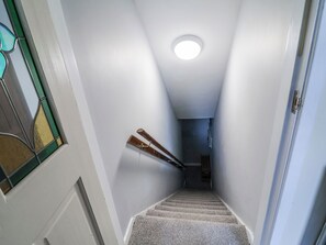 A narrow stairway with a handrail, a stained glass window on the left, and a door on the right. - The Georgian Apartment (Congleton)