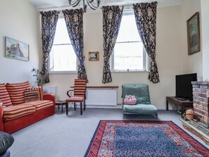 A living room with a sofa, chairs, a television, a fireplace, and patterned curtains. - The Georgian Apartment (Congleton)