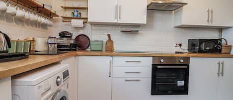 A kitchen with white cabinets, a washing machine, a microwave, and a stove.