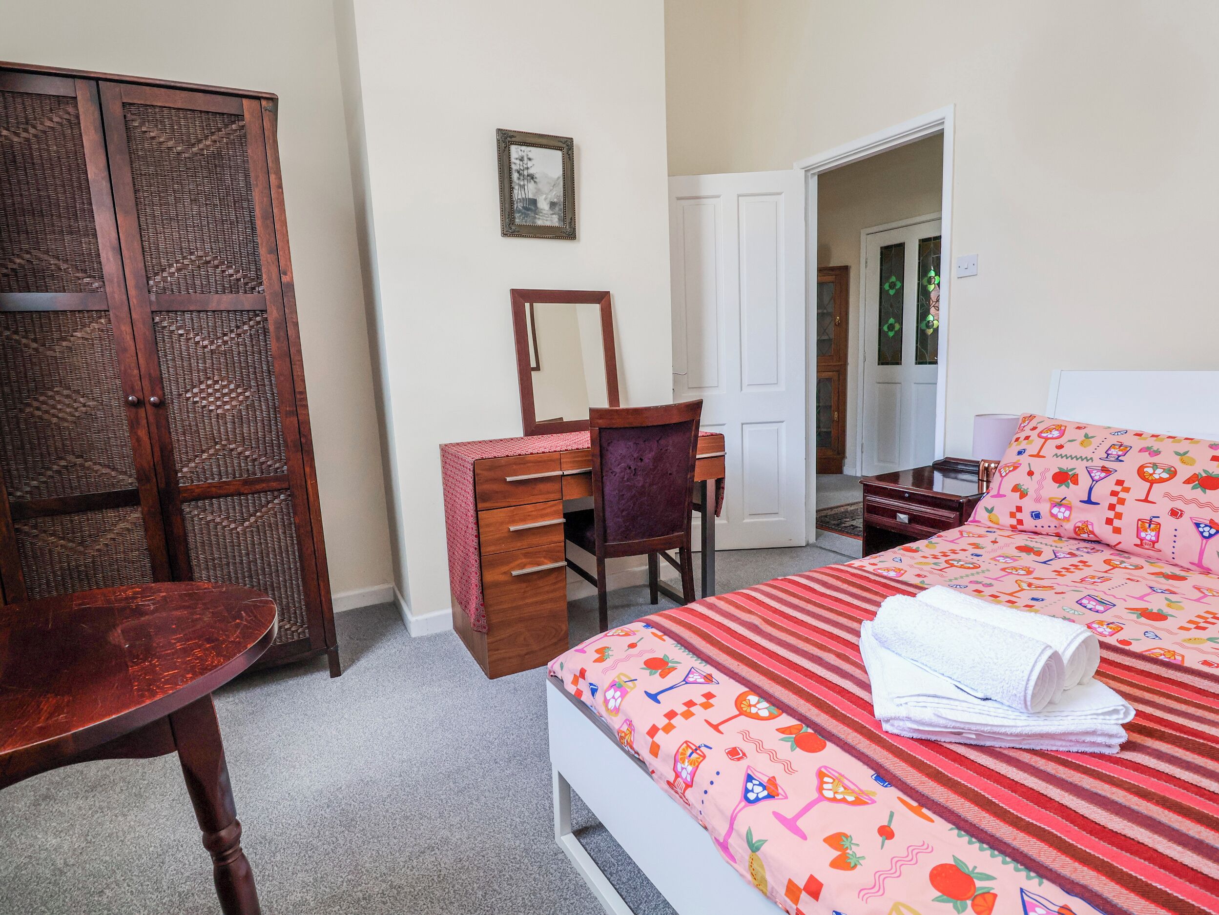 A bedroom with a bed, a dresser, a chair, a mirror, and a door leading to another room.