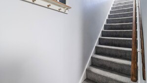 En trappa med steg klädda i matta och träräcken, som leder upp till en liten plattform med en vit vägg och ett fönster med tre rutor.