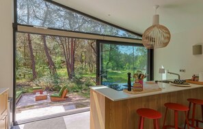 A modern kitchen with a large window, a wooden island with stools, and a hanging pendant light. - De Rode Vos - Enjoying the forest (Lemmer)