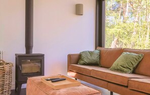 A living room with a sofa, a remote control on a tray, a woven basket, and a wood-burning stove. - De Rode Vos - Enjoying the forest (Lemmer)