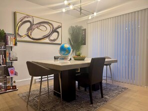 A modern dining area with a round table, chairs, a globe, a bookshelf, and a large abstract painting. - Smart 4BR Comfort Suite Massage Chair YQM Airport (Dieppe)