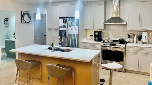 Una cocina moderna con una isla central, electrodomésticos de acero inoxidable y taburetes de bar.