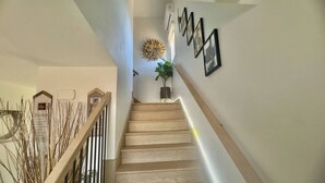 Una escalera de madera con barandilla, que lleva a una plataforma con una planta en maceta y cuadros en la pared.