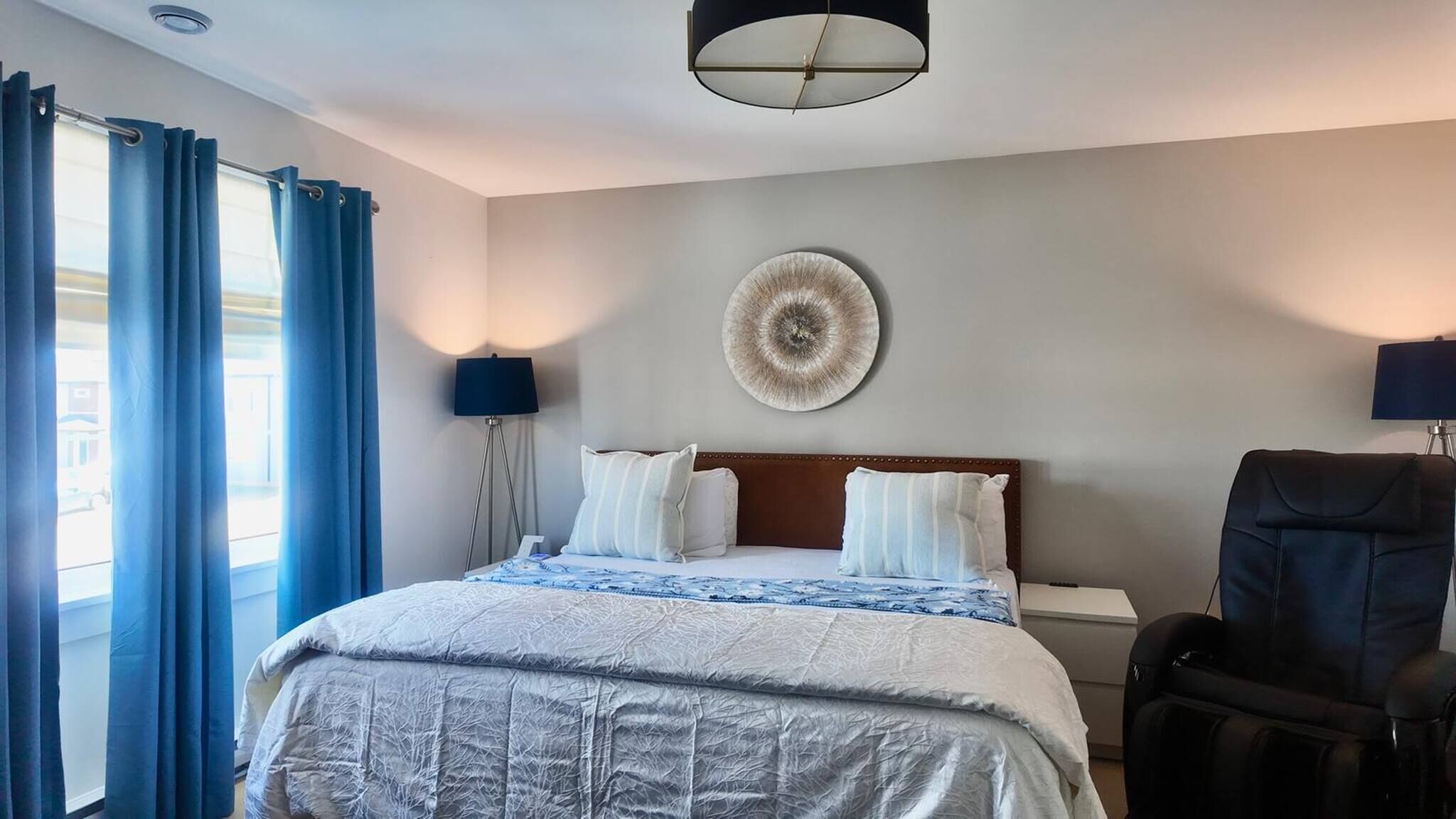 Habitación de hotel con una cama, dos lámparas de noche, una obra de arte circular en la pared y un sillón de cuero negro.