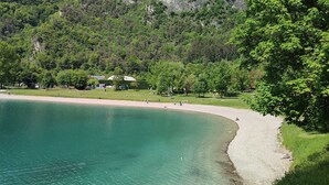 A lakeside view with a curved shoreline, trees, and buildings in the background. - Green Ledro Lake Apartment -A few steps from the Ponale Trail - 800m from the Lake (Molina di Ledro)