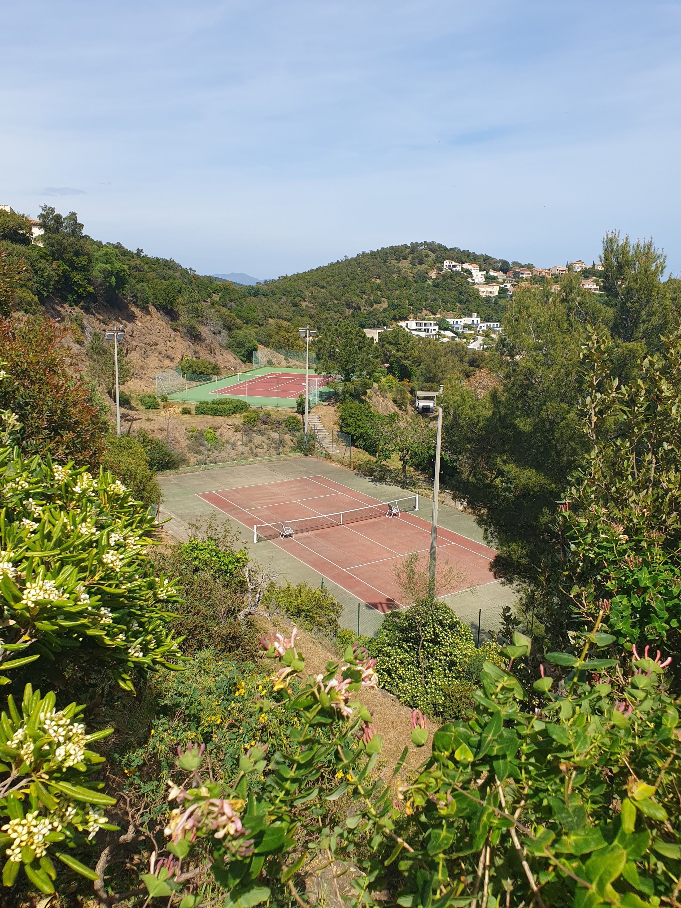 A tennis court surrounded by greenery and houses on a hillside.