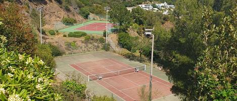 A tennis court surrounded by greenery and houses on a hillside.