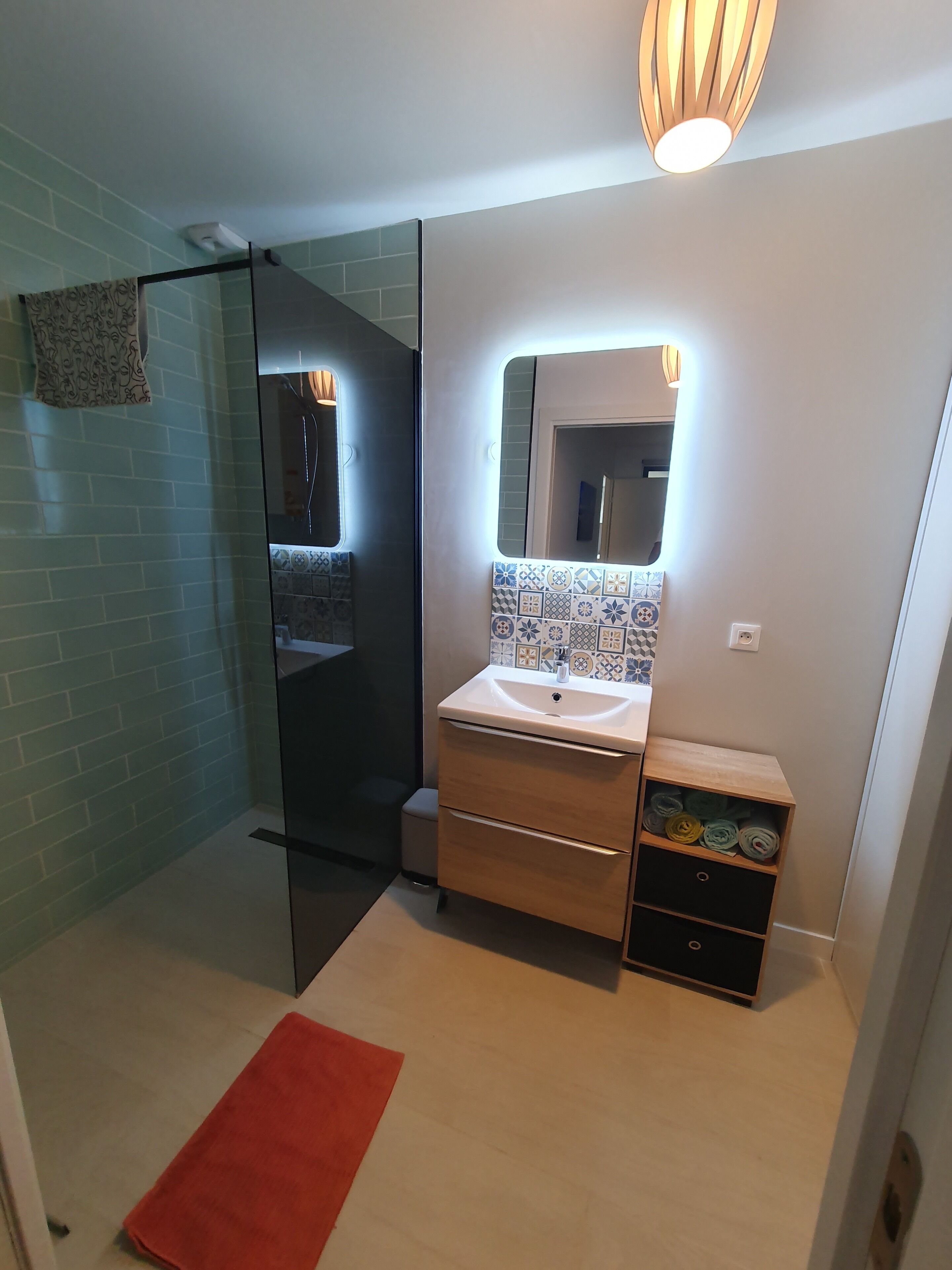 Une salle de bain moderne avec une douche à parois de verre, un lavabo avec un miroir et un petit meuble en bois.