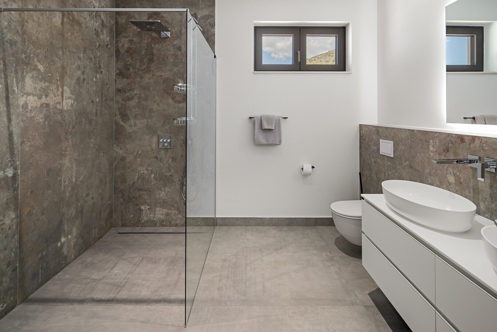 Un baño moderno con cabina de ducha de vidrio, inodoro y un lavamanos amplio.