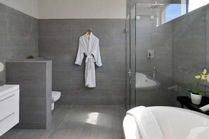 A modern bathroom with a glass shower, a white bathtub, and a white toilet. - Stylish Penthouse Heart of the City by Ctha (Cape Town)