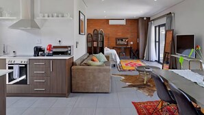 Una cocina moderna con horno empotrado, una zona de comedor con mesa y sillas, un sofá y un televisor.