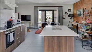 Una cocina moderna con una isla central, una zona de comedor con mesa y sillas, y un balcón con vistas.